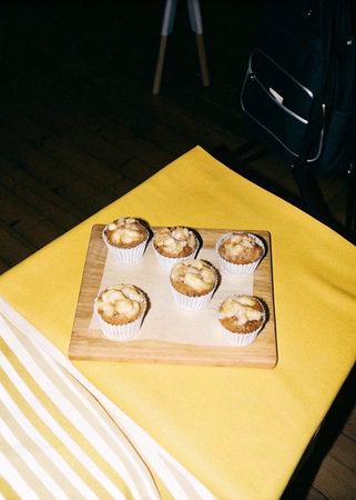 Homemade muffins on a wooden cutting board on a yellow tablecloth