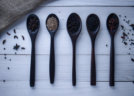 Various spices in wooden spoons on white wooden background. Top view.