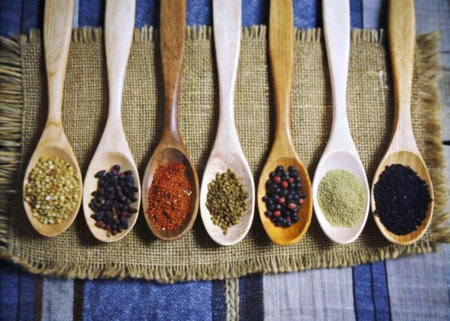 Various spices in wooden spoons on sackcloth background, top view