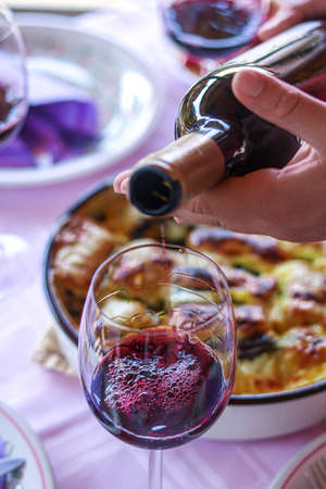 Pouring red wine into glass during lunch time with pink table and cooking pan in a backgroundの写真素材