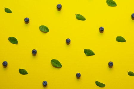Blueberries with leaves laid out as a pattern on a bright yellow background in flat lay style, top viewの写真素材
