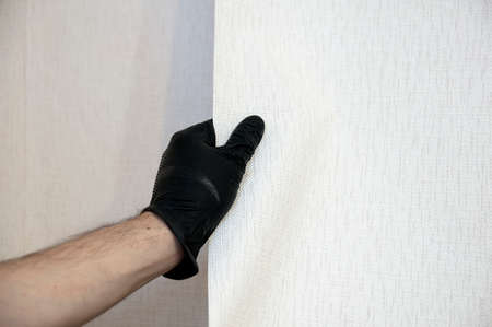 Male hand in black glove tear off old white wallpaper from the wallの写真素材