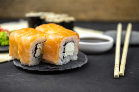 philadelphia maki rolls and eel unagi maki with soy sauce, pink ginger, wasabi on black background,...
