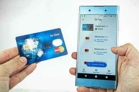 Payoneer card in a hand and Google Pay app on a smartphone. Debit card, money transfer, smart wireless payment concept. Kiev, Ukraine - August, 2020のeditorial素材