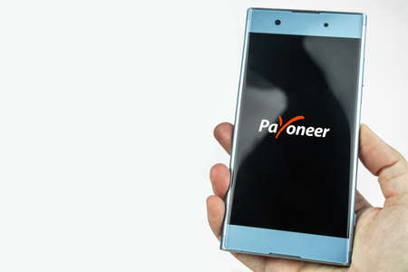 Payoneer card in a hand and app on a smartphone. Debit card, money transfer concept. Kiev, Ukraine - August, 2020のeditorial素材
