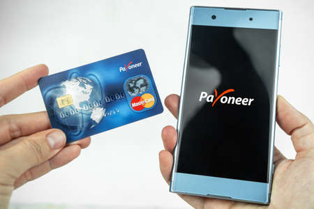 Payoneer card in a hand and app on a smartphone. Debit card, money transfer concept. Kiev, Ukraine - August, 2020のeditorial素材