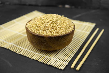brown rice in a wooden bowl on bamboo mat, asian kitchen background on blackの写真素材