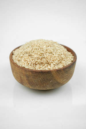 brown rice in a wooden bowl isolated on white, vertical studio shotの写真素材