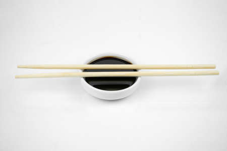 soy sauce in a small white bowl and bamboo chopsticks, isolated on whiteの写真素材