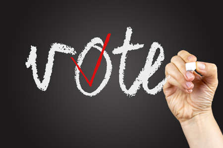 Vote phrase and checkbox on a blackboard, written with white chalk in a hand.の写真素材