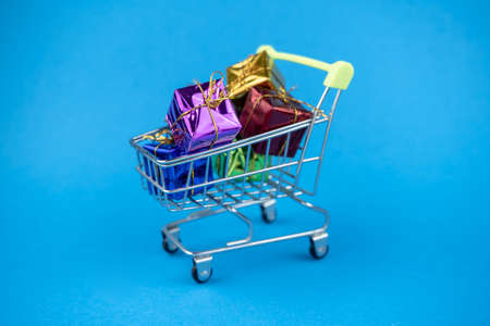 Shopping cart full of minimal present boxes. Gifts for holiday on blue backgroundの写真素材