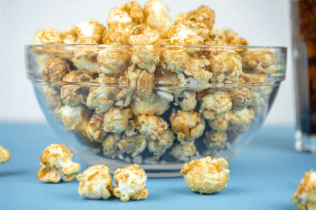 glass of cold refreshing cola soda with ice, glass bowl of fresh popcorn with caramel