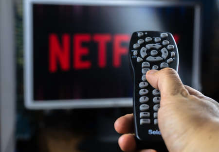 tv remote control in front of tv screen with netflix logo