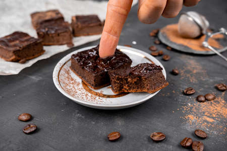 Cocoa brownies pouring with melted dark chocolate cut out to square pieces on a white plate. Black...