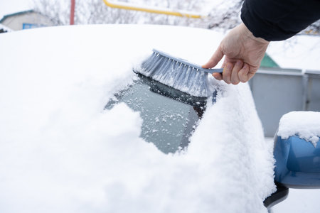 Clearing snow from the car windshield with car brushの写真素材