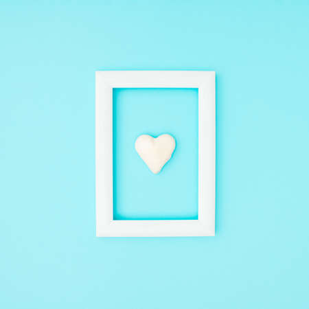 Love background minimal concept. White frame with small heart inside on blue background.