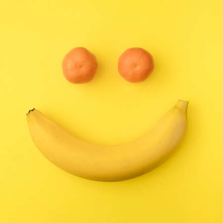 Summer tropical flat lay creative concept. Positive smile face from yellow banana and orange tangerine on a vibrant illuminating background.の写真素材