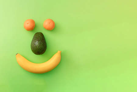 Positive smiley face from banana, avocado  and tangerine on a green background with copy space. Flat lay colorful concept.の写真素材