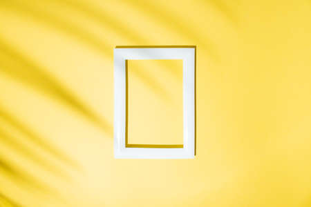 Frame and palm leaf shadow on a yellow background. Tropical summer white frame concept on minimal...