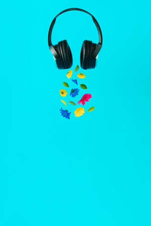 Advertisement idea with black music headphones, colorful summer flowers and green leaves against pastel blue background. Minimal nature concept in vertical orientation.の写真素材