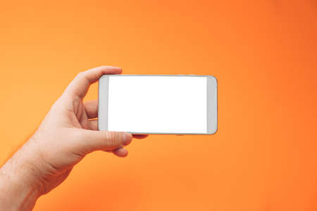 Hand holding white 3d smartphone against orange background. 3D illustration design template background. Top mobile phone message. Advertisement idea. Blank landscape copy space for ad.の写真素材