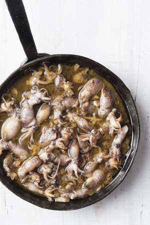 close up of pan of rustic baby squid in garlic and olive oil