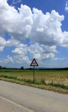 school warning traffic road sign with cloudy sky and fieldの写真素材