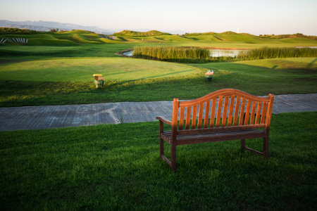 Walkway with bench near golf course over the lake with trees on background at sunsetの写真素材