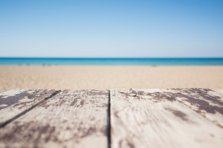 Wooden table on the sandy beach of the sea with old white paint under the blue skyの写真素材