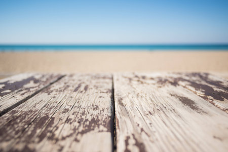 Wooden table on the sandy beach of the sea with old white paint under the blue skyの写真素材