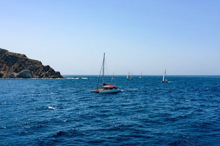Lots of different boats with tourists near Santorini islands in a deep blue sea. Small church on top of the rock. Greece in summer.の写真素材