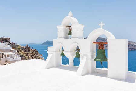 Green bells on roof of the church with lots of tourists in the background and picturesque view to the island in the Oia village at Santorini, Greece.の写真素材