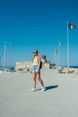 A young beautiful girl in a t-shirt, denim shorts, white sneakers in sunglassesの写真素材