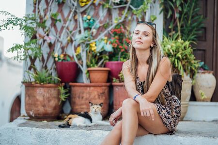 Beautiful young woman sitting next to the cat on a white stairs.の写真素材