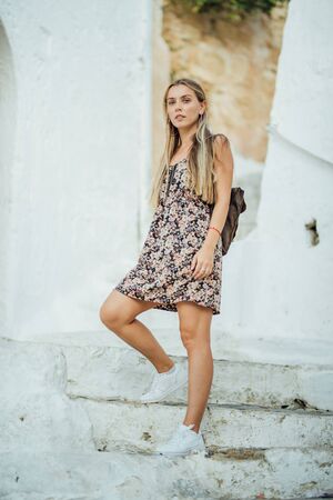 Young beautiful girl in flower dress posing on white stairs in Lindos city, Greeceの写真素材