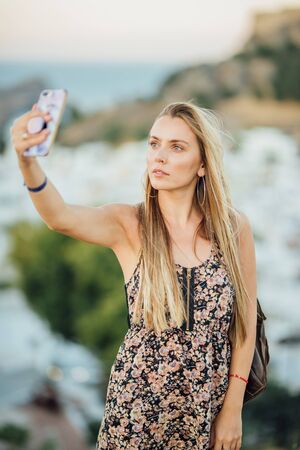 Beautiful young woman making a selfie with a smartphone on top of Lindos villageの写真素材