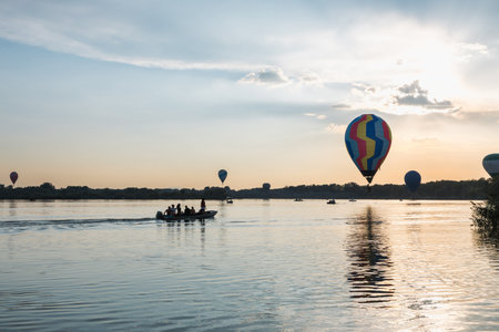 Colorful hot air balloons flying over lake at sunsetの写真素材