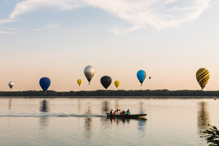 Colorful hot air balloons flying over lake at sunsetの写真素材