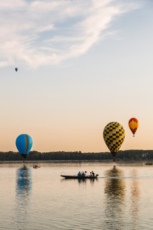 Colorful hot air balloons flying over lake at sunsetの写真素材