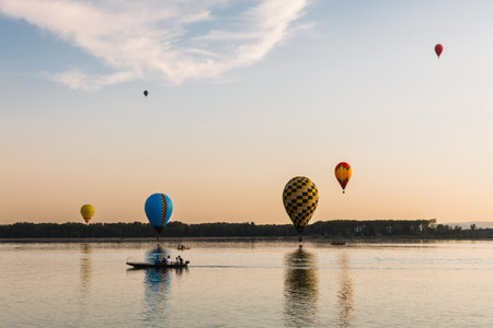 Colorful hot air balloons flying over lake at sunset