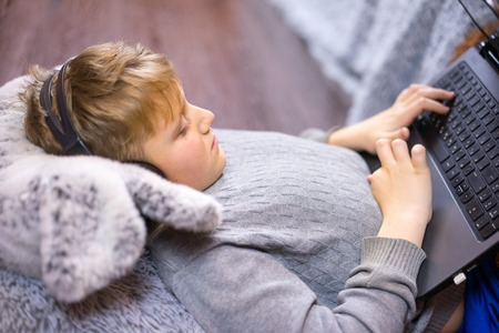 The child lies on the floor and plays on the laptop.