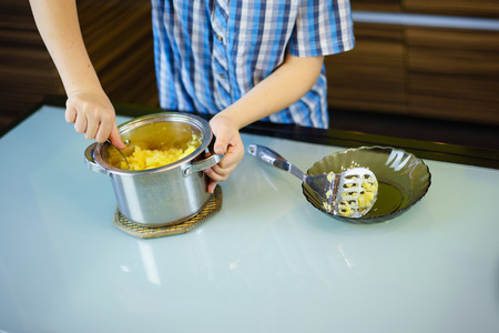 The boy cooks mashed potatoes in the kitchen. Close-up.の写真素材