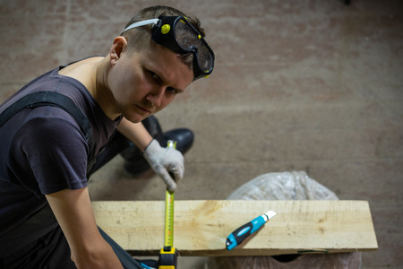 A worker at a construction site where repairs are underway, measures with a pencil how much to cut...