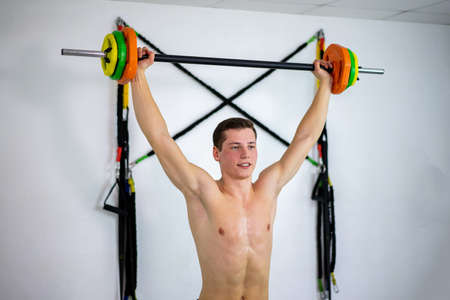 A young guy with a beautiful body raises the barbell in the gym where  classes are held.