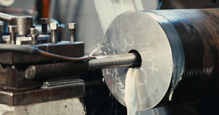 A close-up of a metal workpiece clamped in a rotating chuck of a machine tool. Steel drill and...