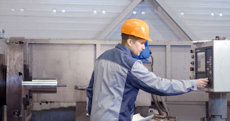 Portrait of a young worker in a helmet at a large metalworking plant. An engineer maintains machines...