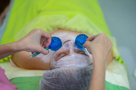 Skincare concept. Close up portrait of relaxed young girl getting massage with cold blue balls with...