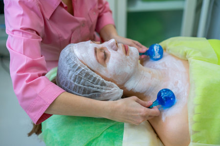 Natural makeup. A girl receives a massage with cold blue balls with a special liquid in a beauty salon. Skin care concept. Clean healthy skin.の写真素材