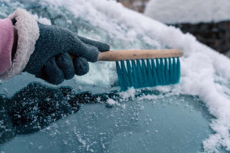 Woman taking care of automobile removing ice with brush outdoors. Removing snow from windshield. Scraping frozen ice.の写真素材