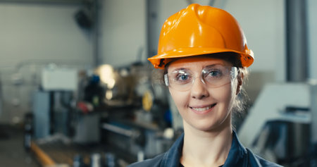 Portrait of a beautiful smiling female engineer in a protective vest and hard hat with goggles. Professional woman working in a modern manufacturing plant. CNC objectの写真素材